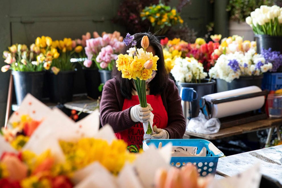 A woman surrounded by flowers with a bouquet hiding her face