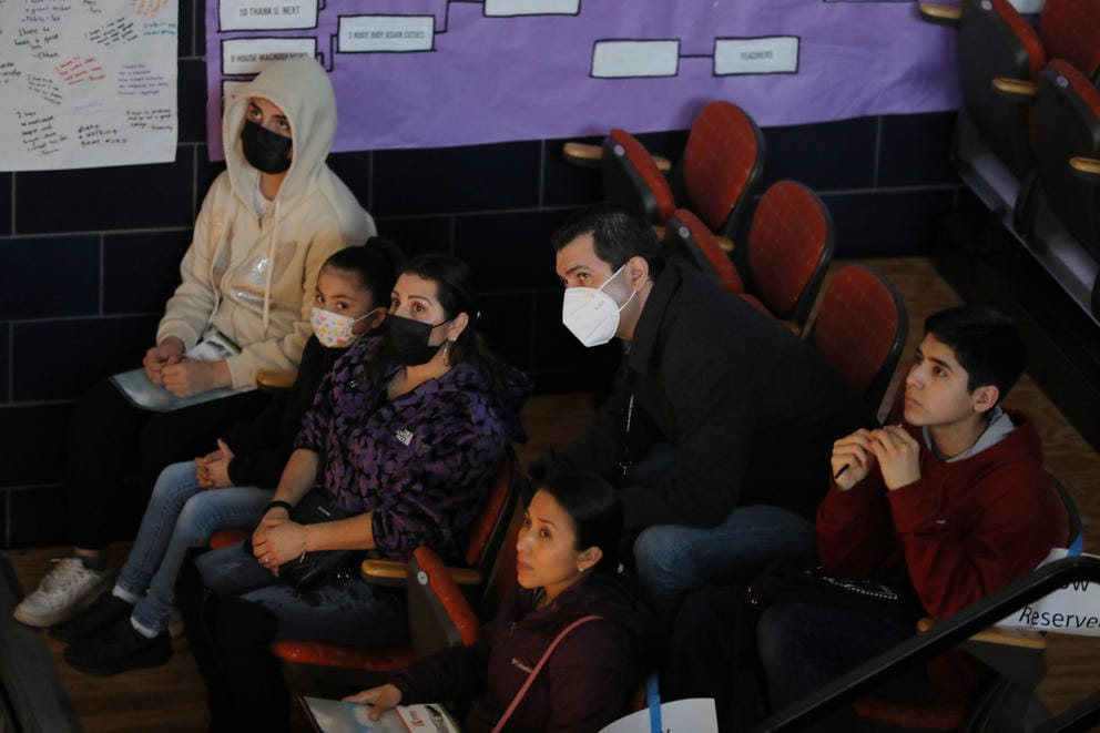 A language translator assists two families at a high school orientation.