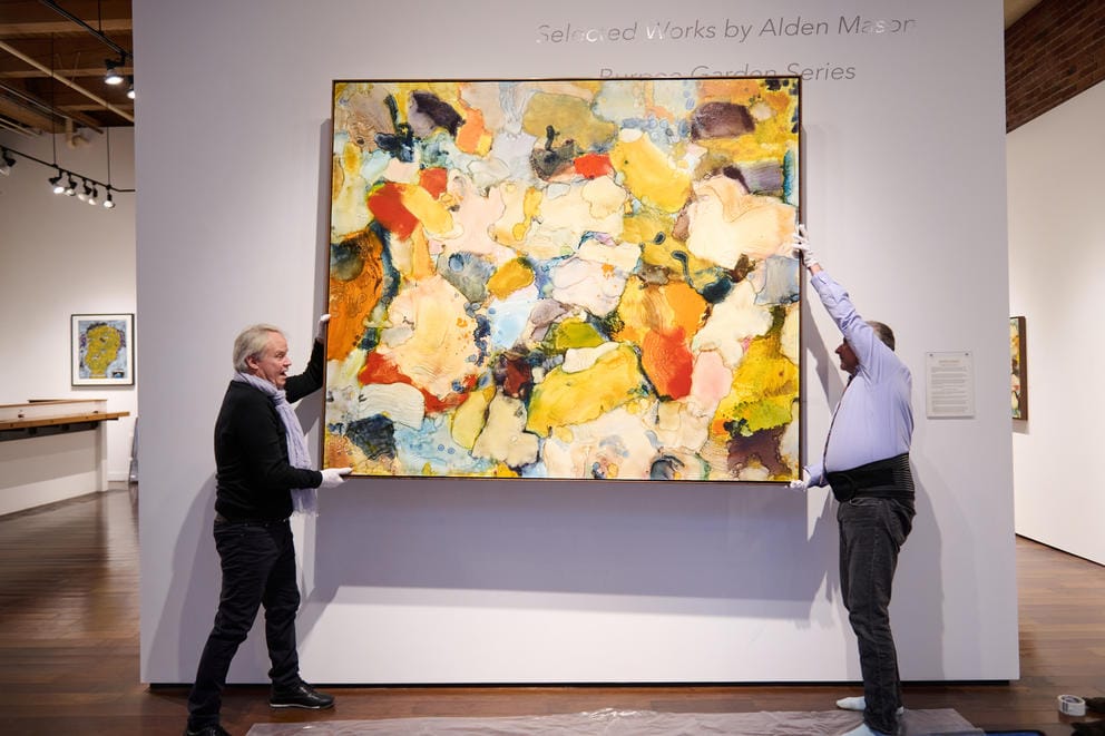 Two people take a bright painting off the wall