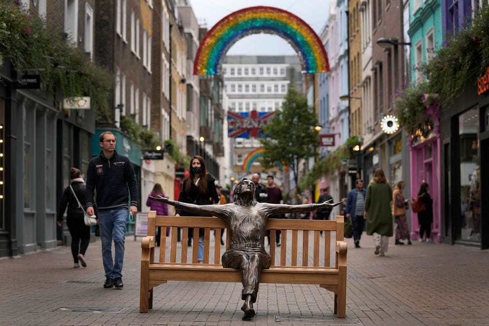 a busy plaza in london with people walking around a bronze statute of john lennon
