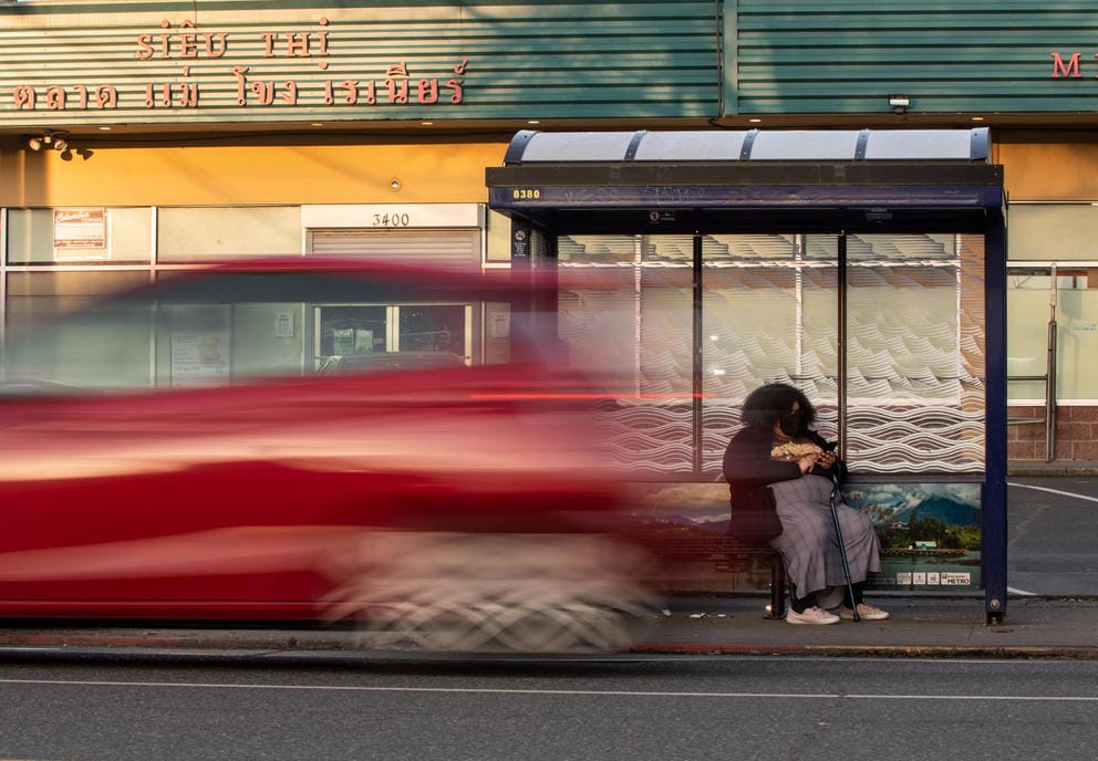 A person waits at a bus stop on the corner of Rainier Avenue South and South Walden Street