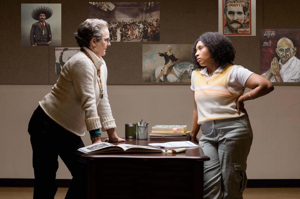 A white woman and a Black woman glare at each other across a table in an academic setting