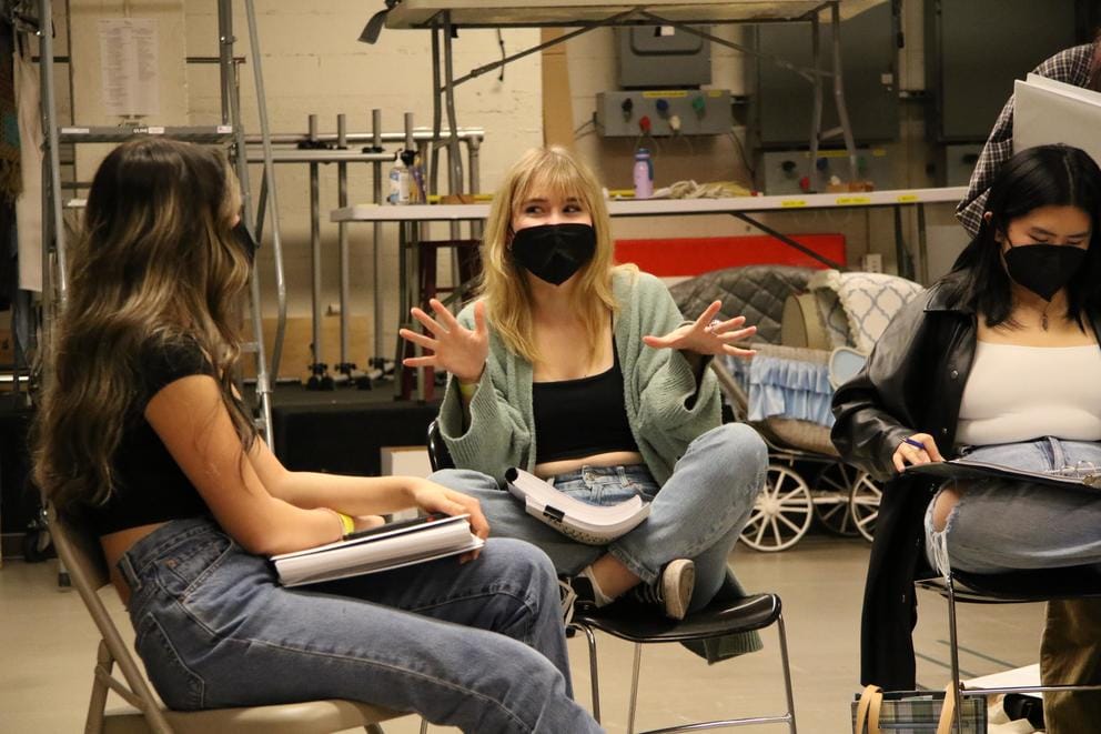 Three girls sit in a circle with scripts in their laps