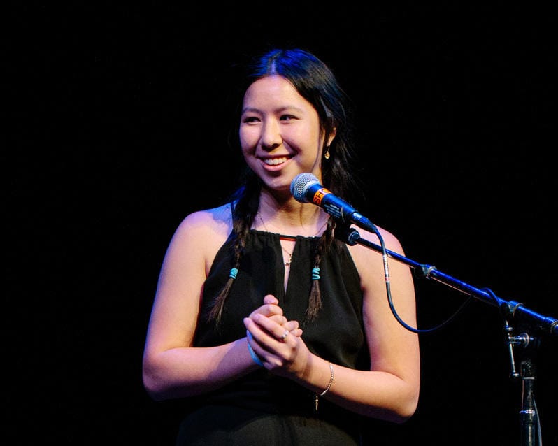 A girl standing and smiling with her hands holding each other