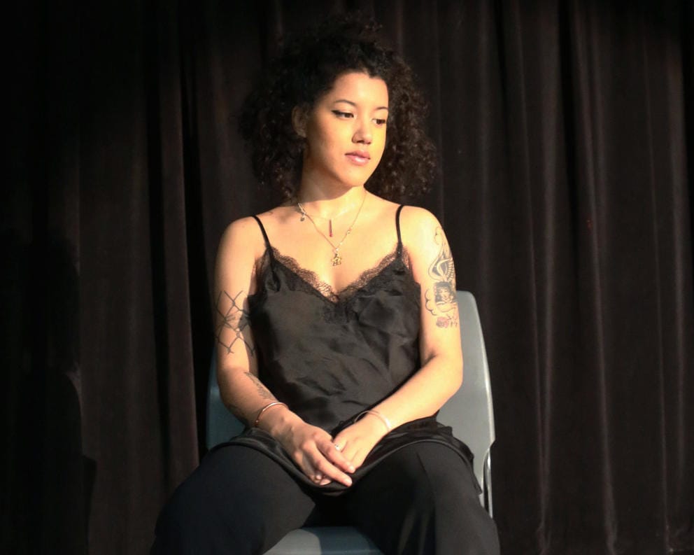 A girl sits facing down with her hands clasped together in her lap