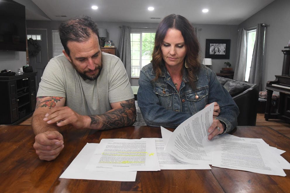 Two adults sit at a dining room table looking through the a stack of paper.