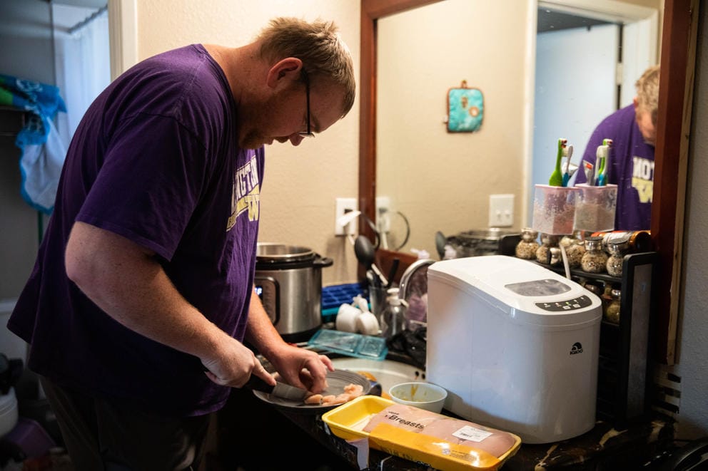 Ryan Blackledge cuts chicken at the bathroom sink for their family dinner in their apartment.