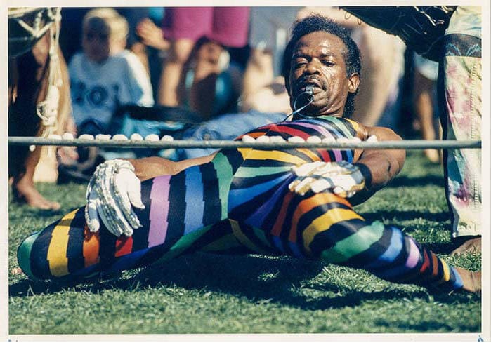 a man in rainbow tights pushes his body under an incredibly low limbo pole