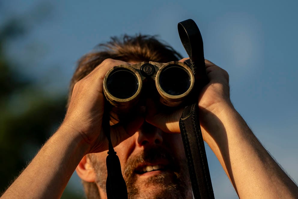 A person peers through binoculars into the distance.