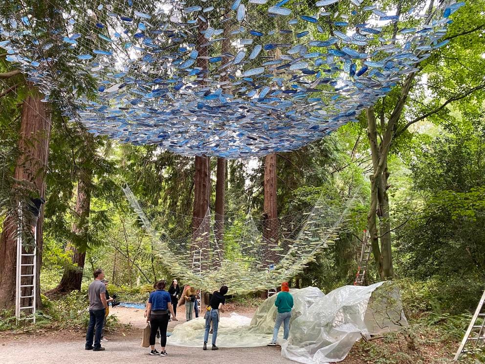 photo of an art installation in progress, with a net filled with green resin pieces is being raised up