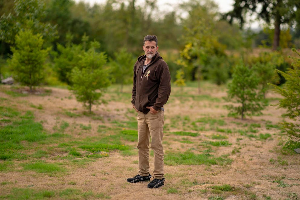 A man stands outside surrounded by patches of grass and trees