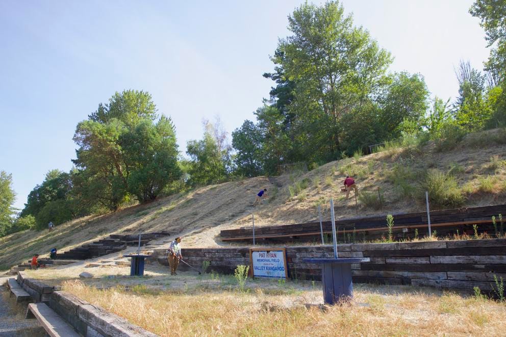 people with landscaping equipment work on a steep hillside next to a sign