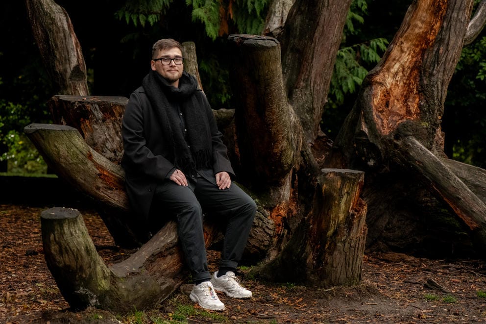 Daniel Lugo sits for a portrait among a stand of trees.