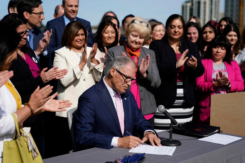 Lawmakers, including primary bill sponsor state Sen. Karen Keiser clap as Washington Gov. Jay Inslee signs bill to protect abortion pill access