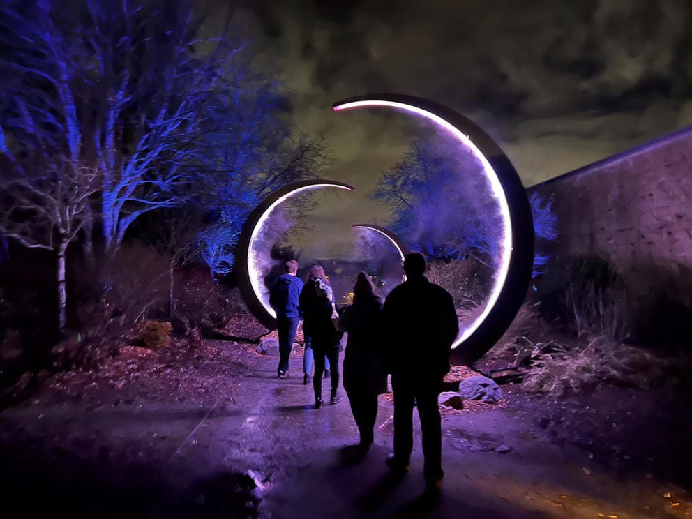 silhouettes of people lining up through an outdoor walkway illuminated by purplish light