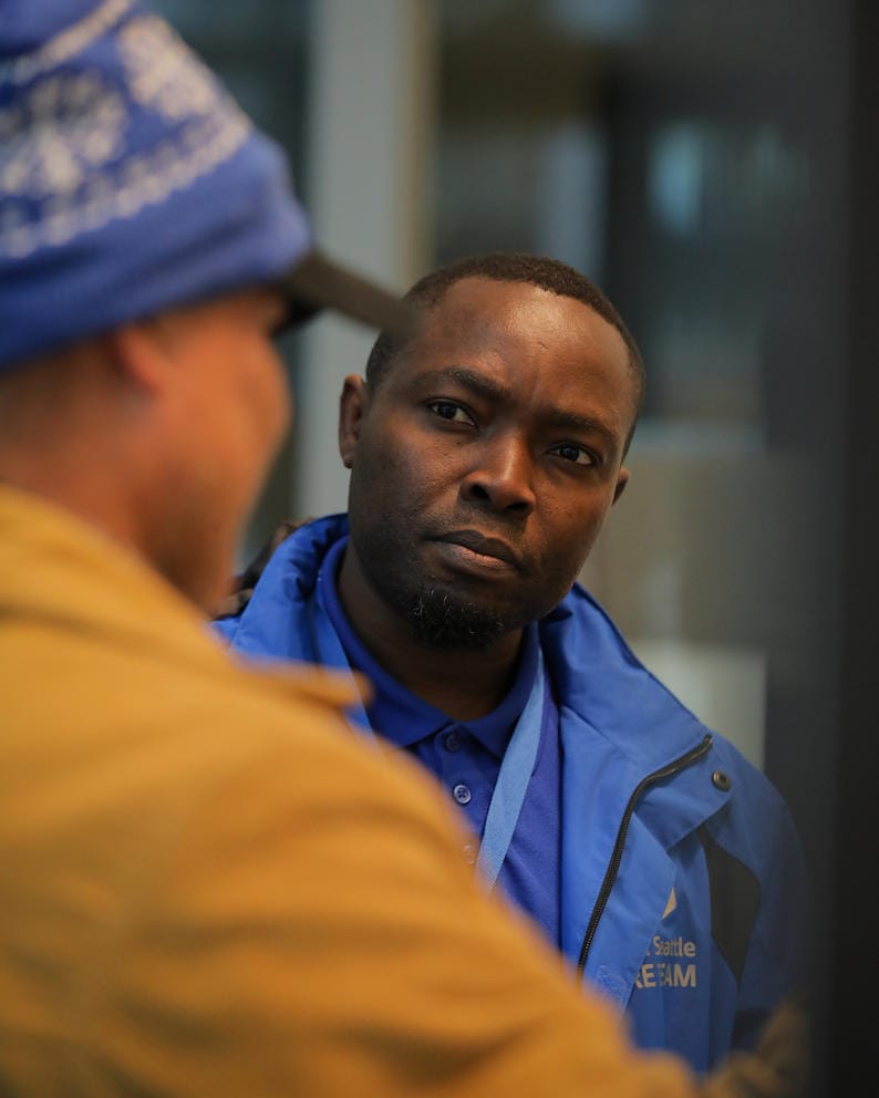 Abdillahi Mohamed listens to a man wearing a hat and yellow jacket whose back is turned to the camera
