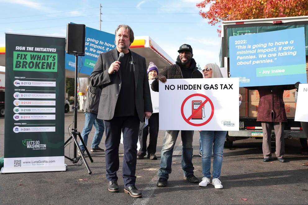 A man with a microphone stands with a group of demonstrators holding signs