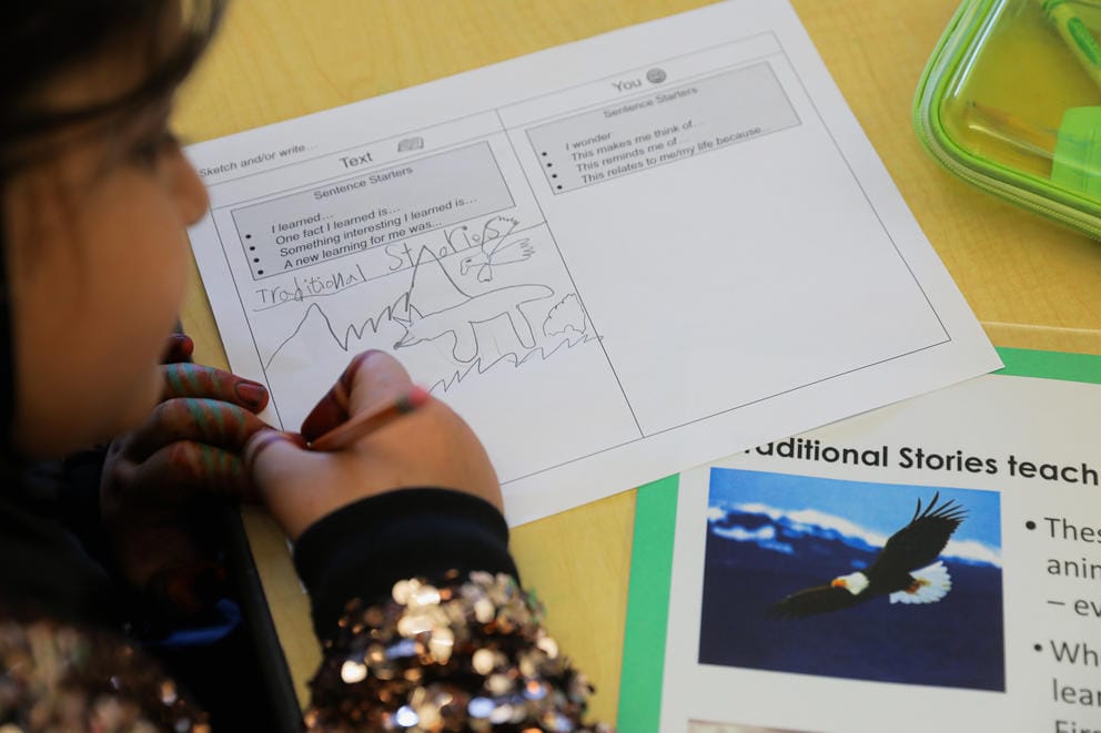 A student draws on a piece of paper on her school desk