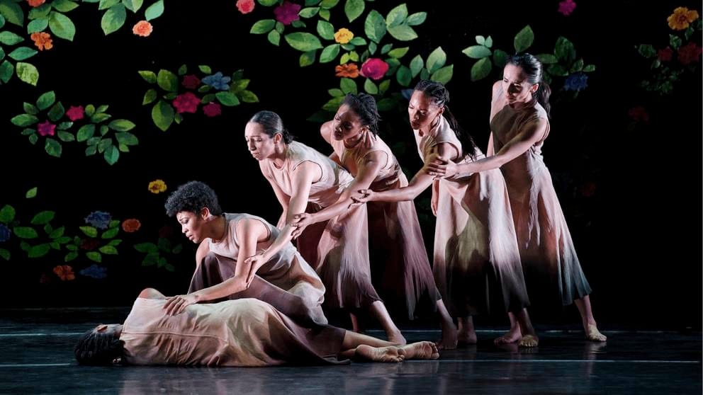 photo of six female dancers on stage in long dresses, each bending over in a line
