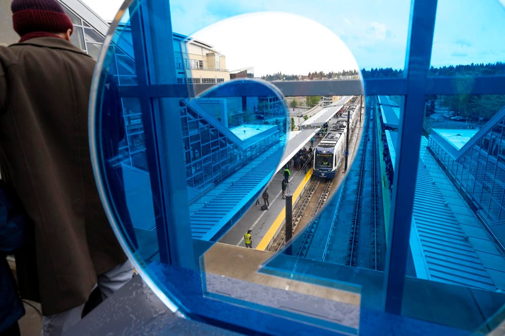 Tracks run under a pedestrian overpass behind a window that with a