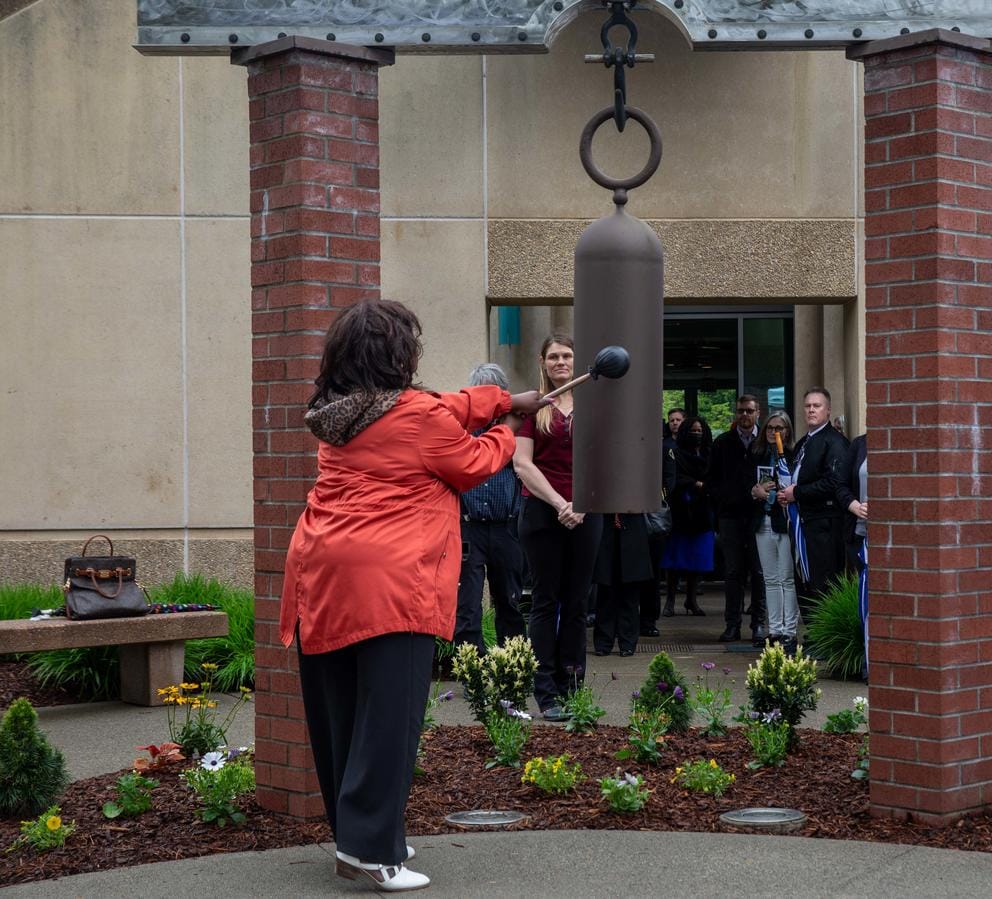A women in a red coat hits a bell with a mallet.
