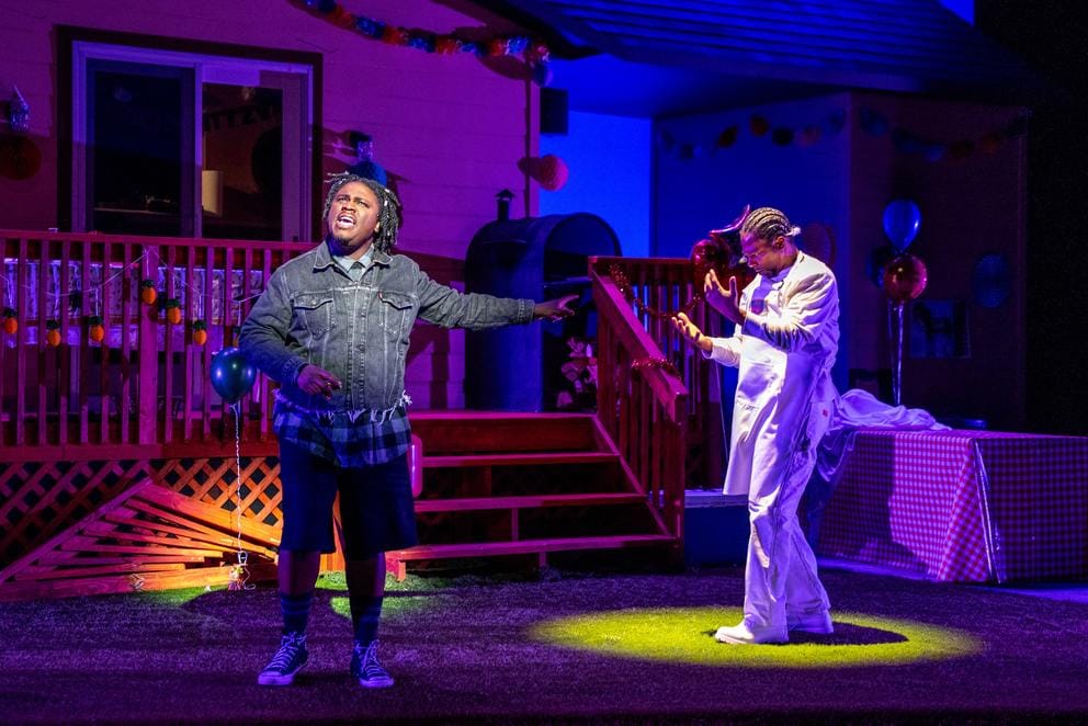 photo of a stage scene, a darkly lit backyard BBQ with two figures talking, one in a circle of light