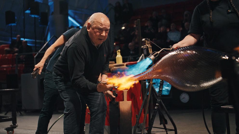 film still of an older man actively moving molten glass in a swooping motion