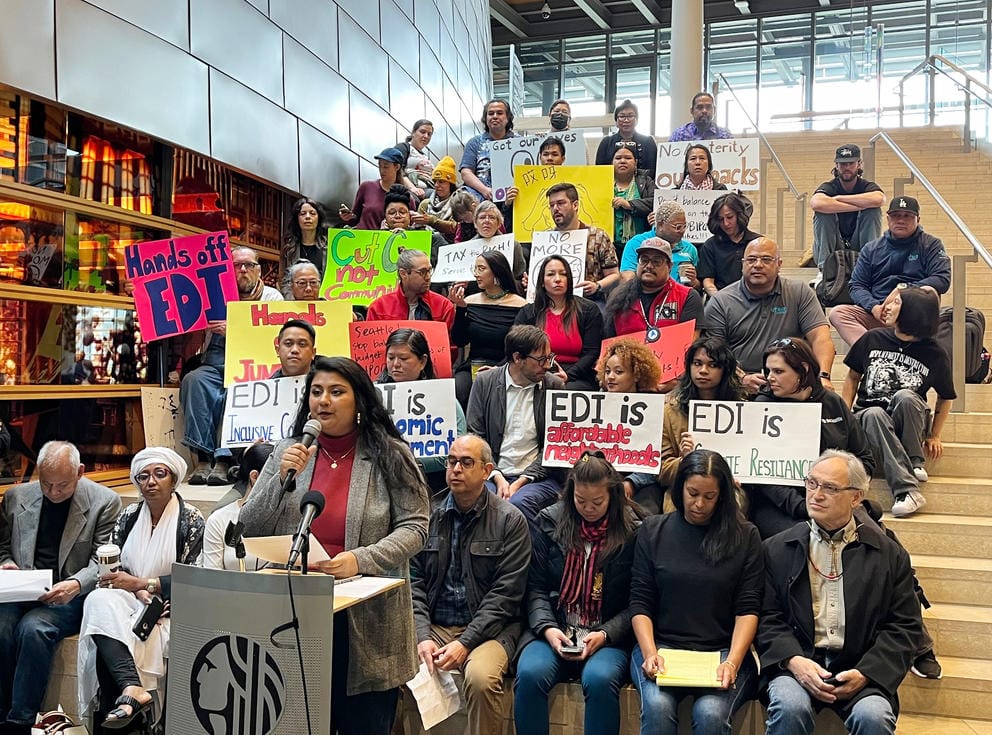 a group of people sit on the steps inside city hall holding signs