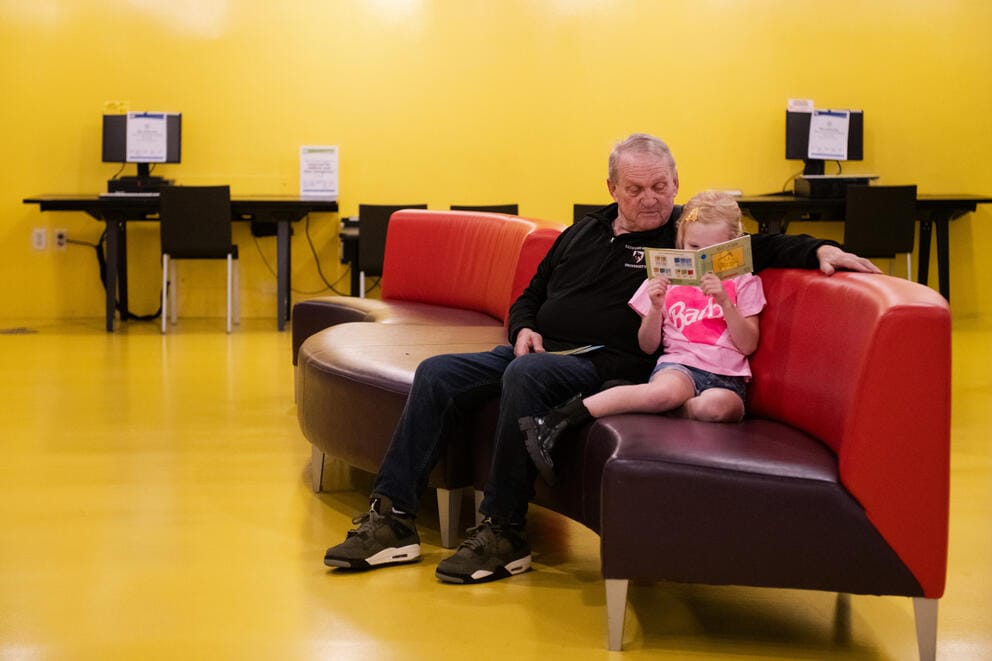 Sam Coe reads a library book next to his granddaughter, Simone in the Central Library Children's Center