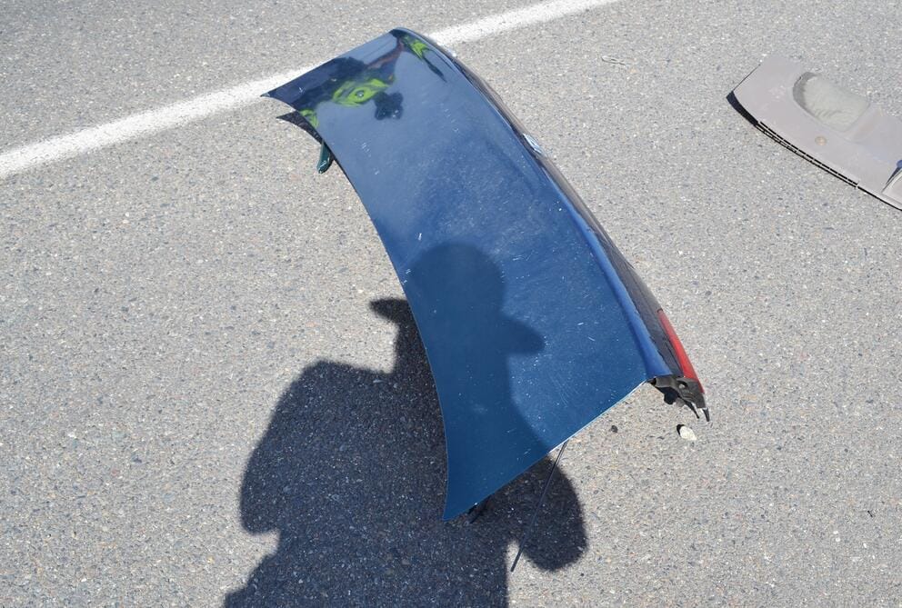 the lid of the Honda's trunk lies strewn in the road; the shadow of a state trooper taking a photo