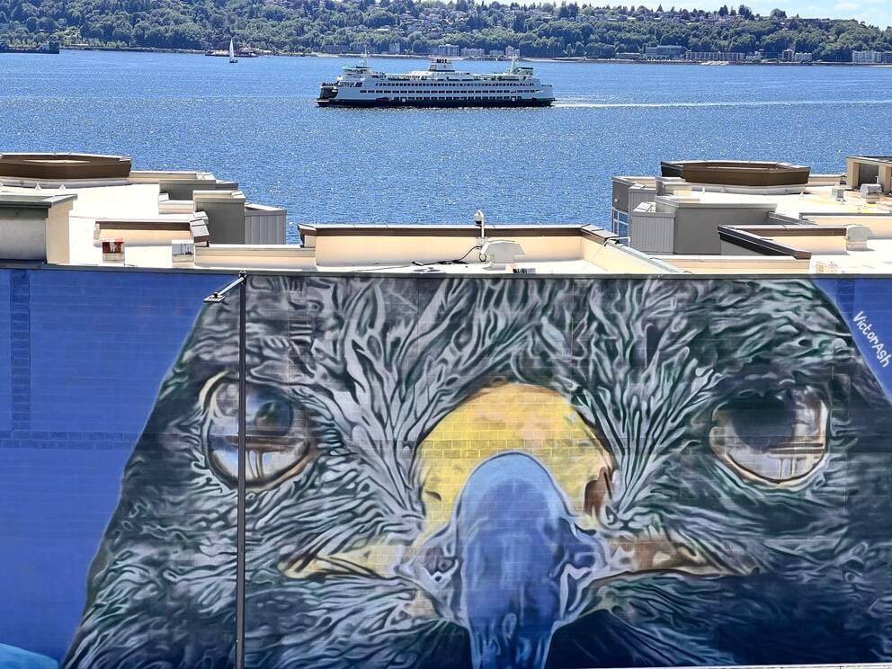photo of a large mural featuring a giant osprey head, with bay and a ferry in the distance