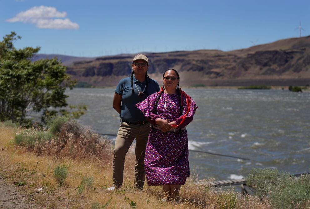 Two people stand in front of a river.