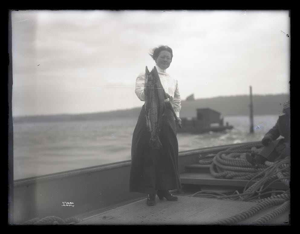 vintage black and white photo of a 1900s woman brandishing a large dead fish