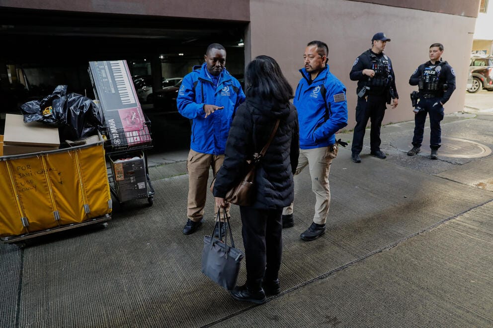 two men with blue care team jackets speak with a woman