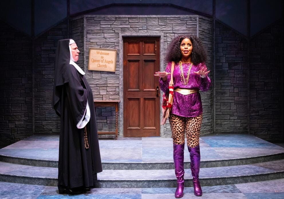 photo of two women acting on stage, one in a nun's habit, the other in a pink and leopard print outfit