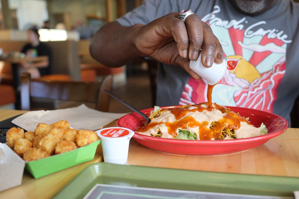 A close up of a hand pouring hot sauce over a taco salad