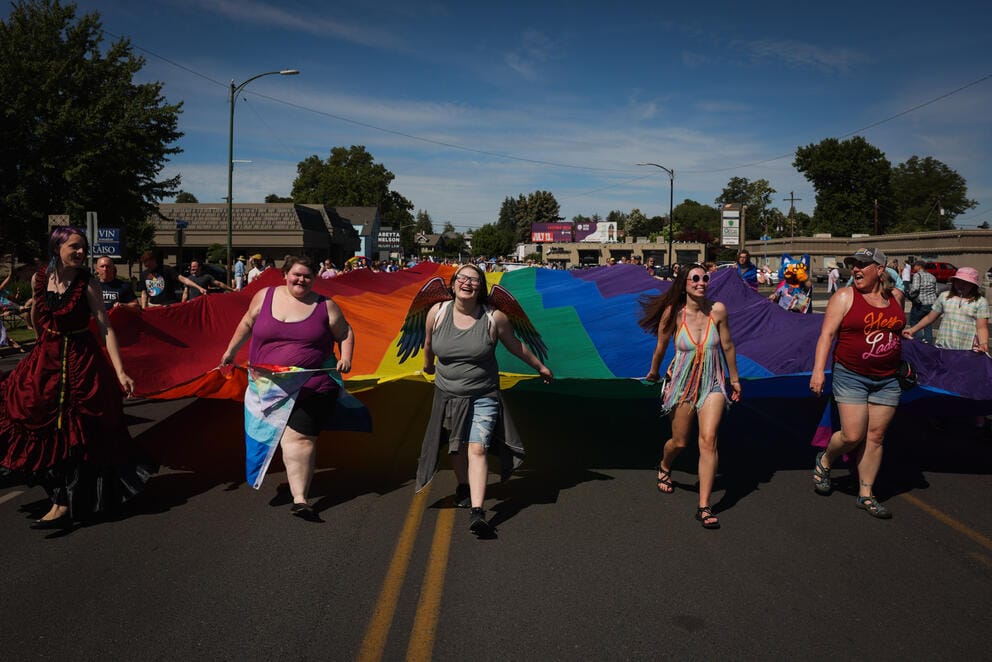 People walk down the street holding a giant Pride flag