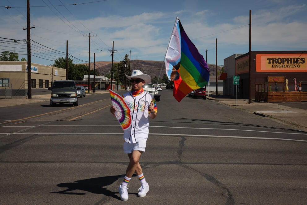 A man holding a rainbow flag stands in the street