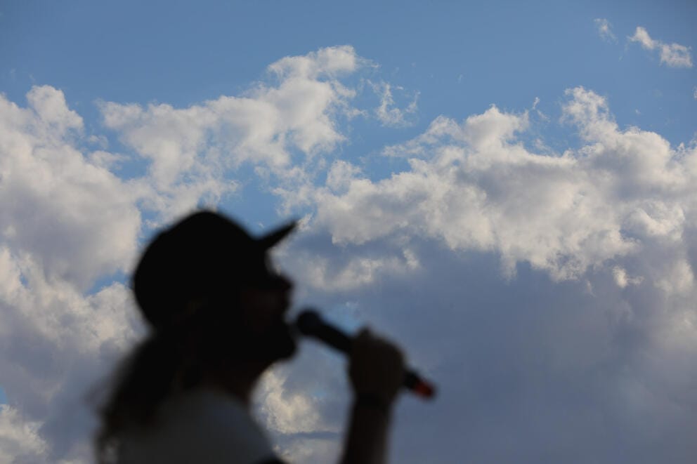A silhouette against the sky of a man holding a microphone