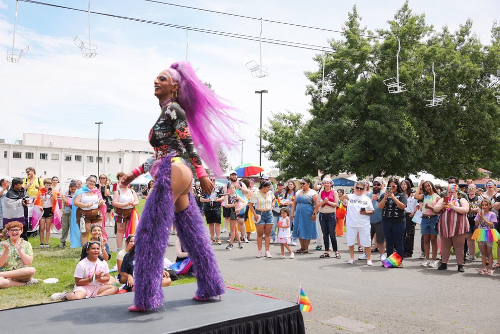 A drag queen wearing all purple and a purple wig performs on stage for a group of people