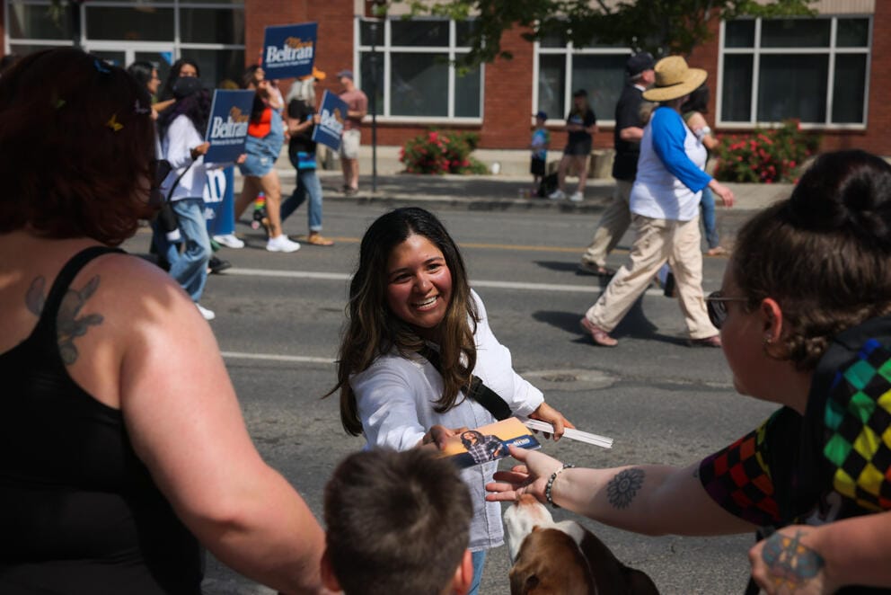A smiling woman hands out a flyer to people on the street