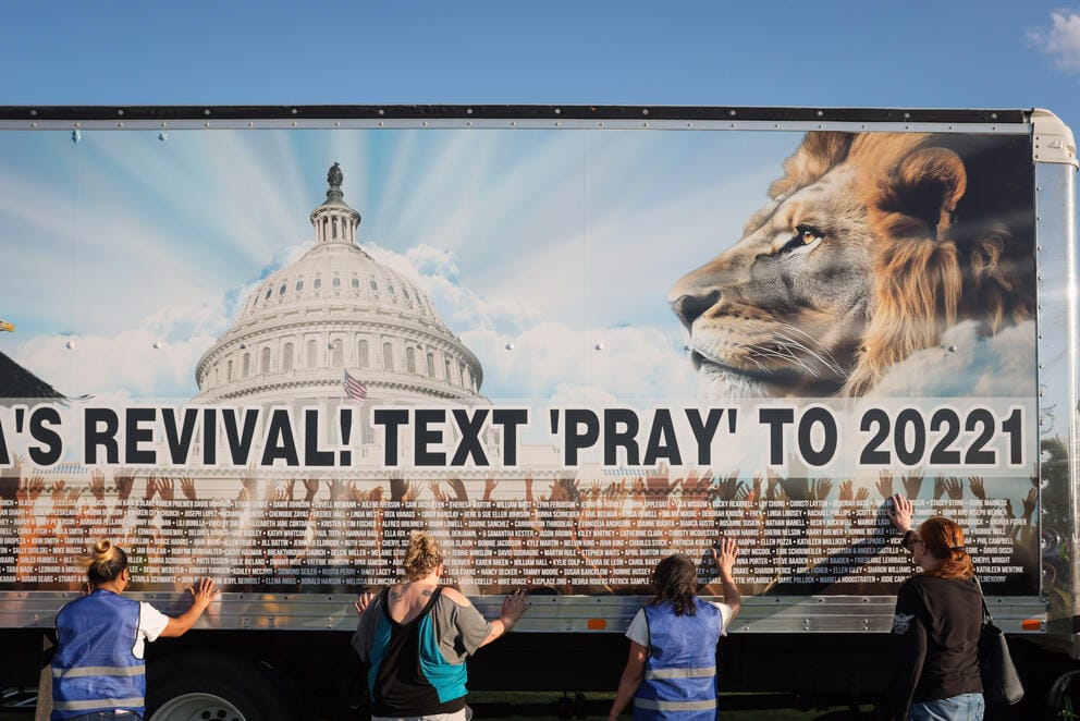 Four people hold their hands on a truck with a picture of a lion and the US Capitol Dome on it. The truck reads