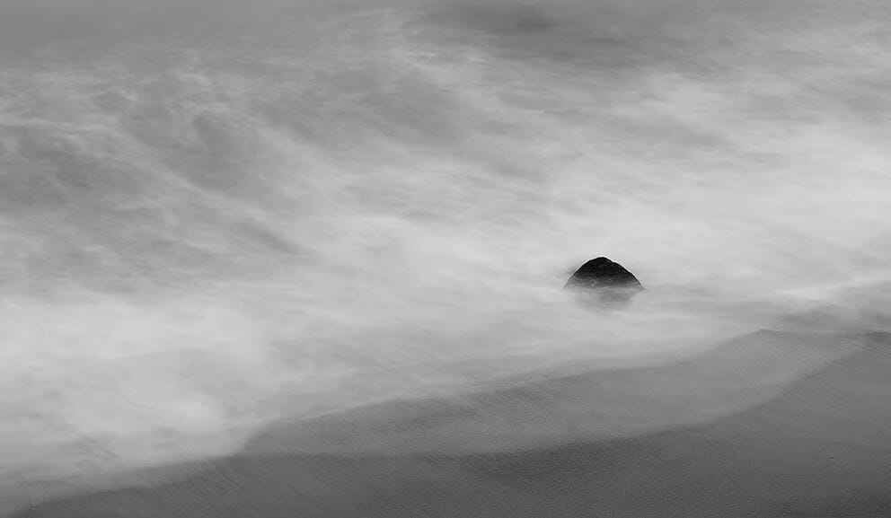 black and white fine art photography shot of a solitary rock formation on a beach in the fog
