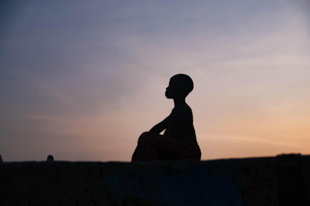 still image from a film, a seated person seen in silhouette against the sunset
