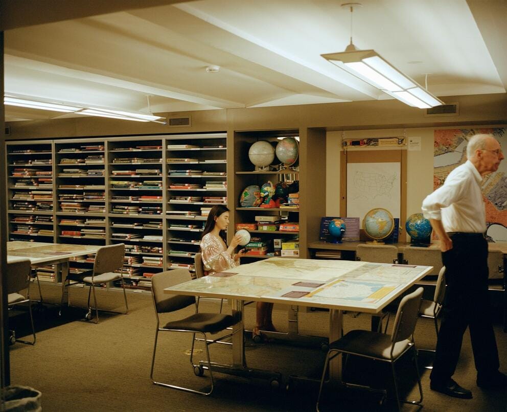 fine art phot of a grown woman in an elementary school classroom, at right an older man walks out of the frame