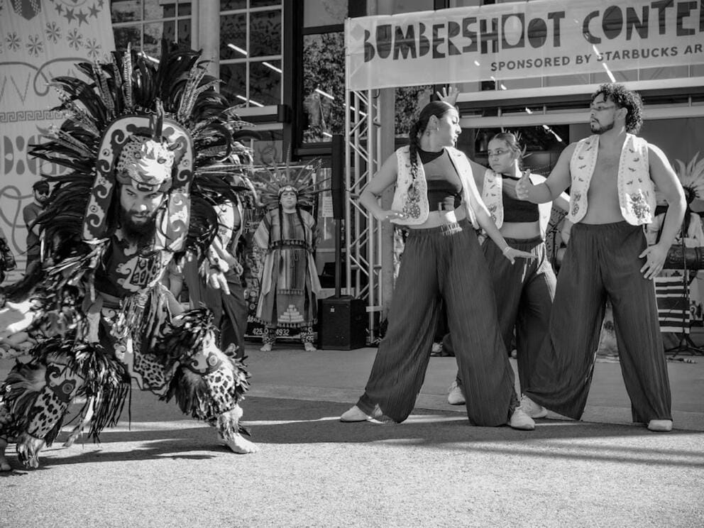 black and white image of an outdoor setting with three dancers, one dressed in a traditional costume