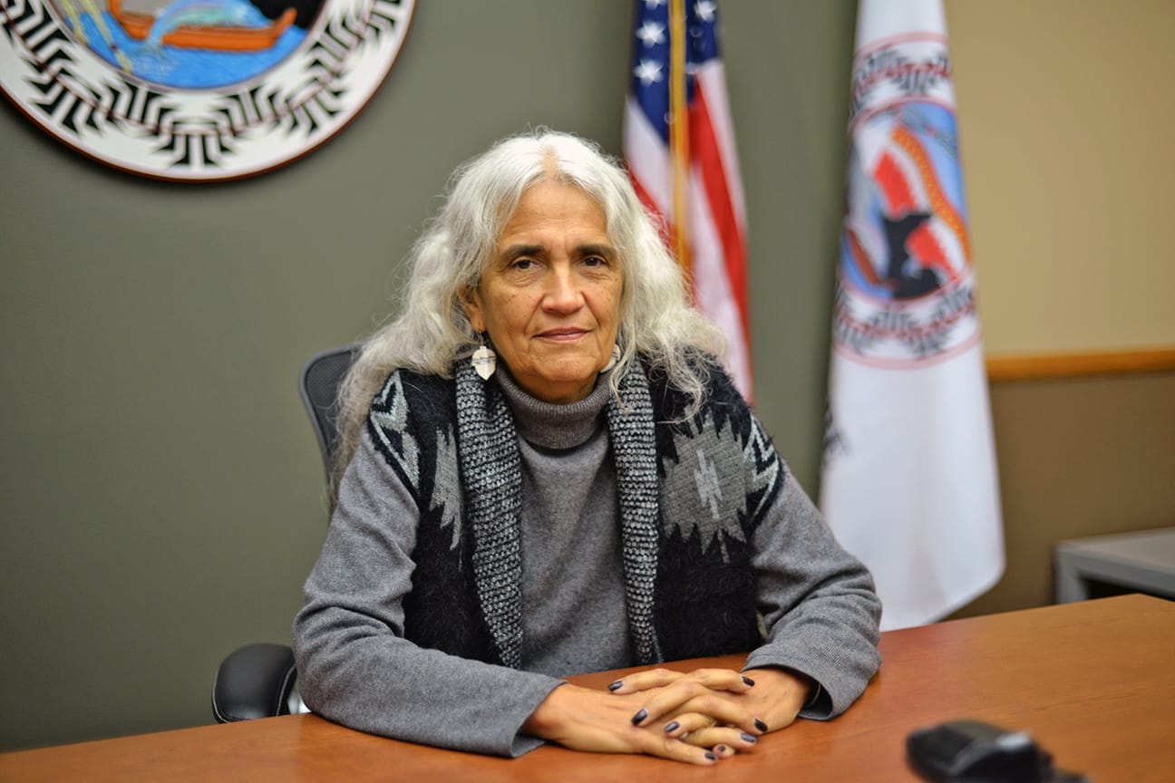 A casually dressed person poses for a photo behind a dais in a courtroom.