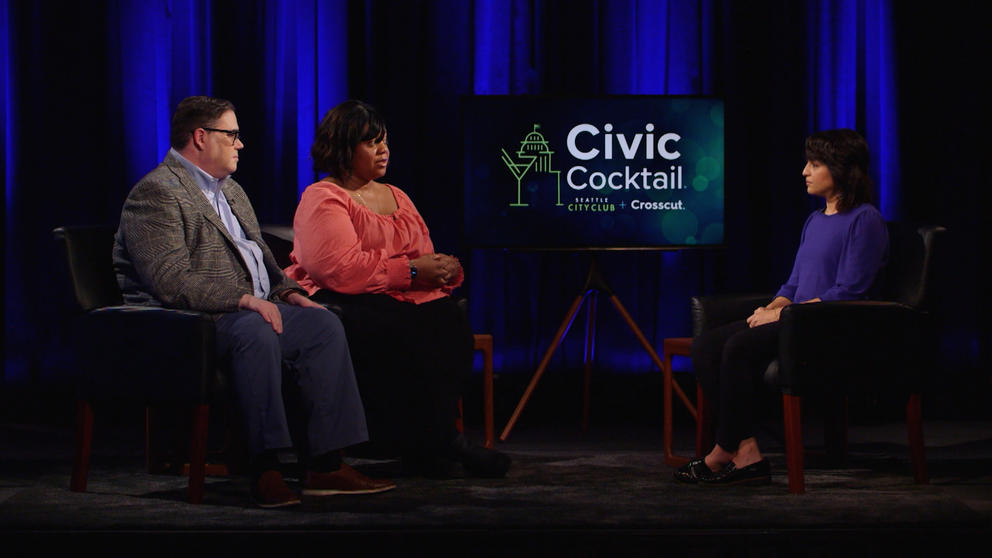 Three people seated on a stage speaking to one another.