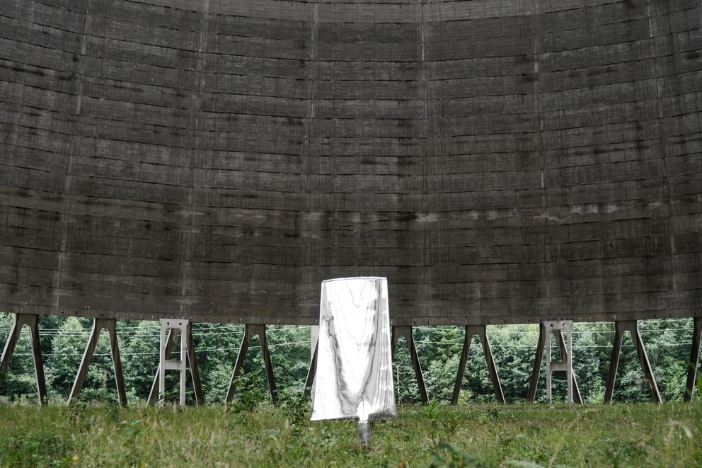 a single chrome blade stands in the grass below a massive structure