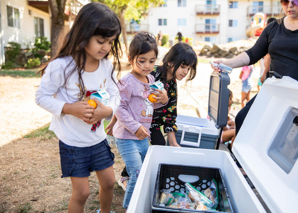 Three children pick up food from a cooler.
